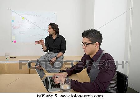Stock Photography - Young men at work, one man using laptop. Fotosearch