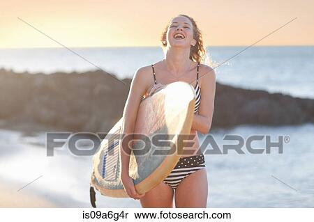 Stock Photography - Young woman carrying surfboard on beach. Fotosearch