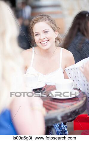 Stock Photograph - Young woman chatting with friends at a cafe. Fotosearch