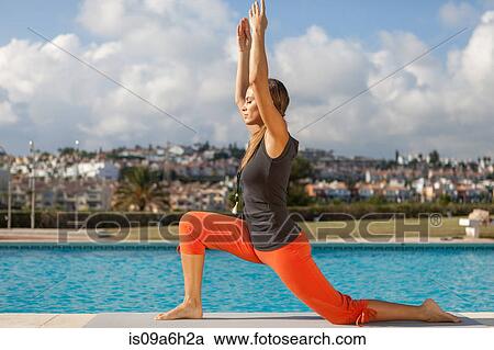 Stock Image - Young woman doing yoga at poolside. Fotosearch