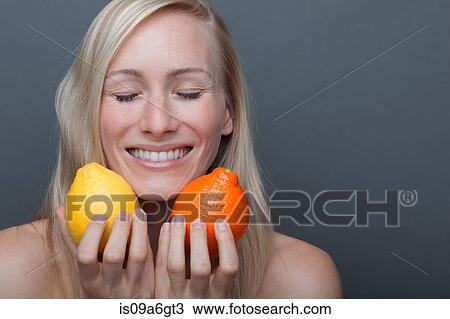 Stock Image - Young woman holding orange and lemon, eyes closed. Fotosearch