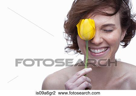 Stock Image - Young woman holding yellow tulip with eyes closed. Fotosearch