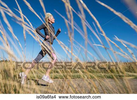Picture - Young woman jogging, view through grass. Fotosearch