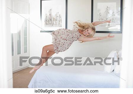 Stock Image - Young woman jumping on bed. Fotosearch