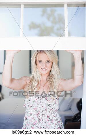 Stock Image - Young woman looking through window. Fotosearch