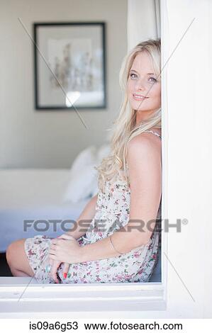 Stock Image - Young woman looking through window. Fotosearch