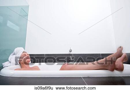 Stock Photograph - Young woman lying in bath with eyes closed. Fotosearch