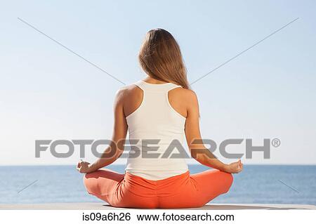 Stock Photograph - Young woman meditating by sea rear view. Fotosearch
