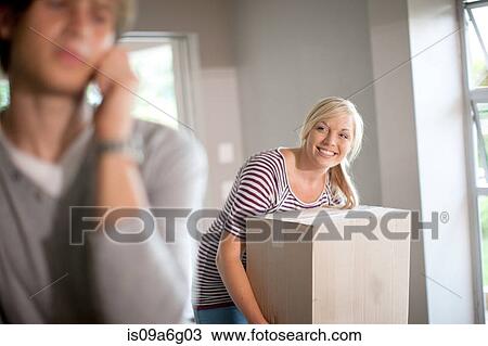 Stock Image - Young woman moving house carrying box. Fotosearch