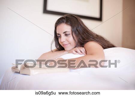 Stock Photograph - Young woman on bed reading book. Fotosearch