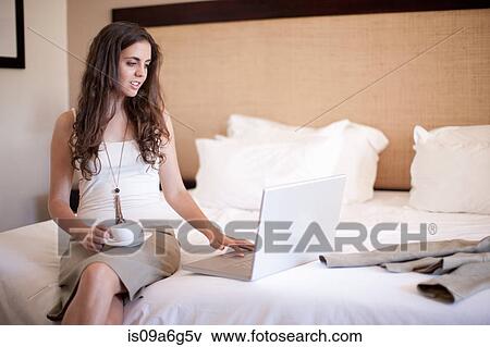 Stock Photo - Young woman on bed using laptop. Fotosearch