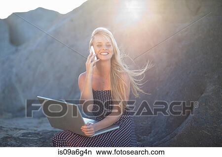 Young woman on rocks with laptop using cell phone View Large Photo Image Picture - Young woman on rocks with laptop using cell phone. Fotosearch