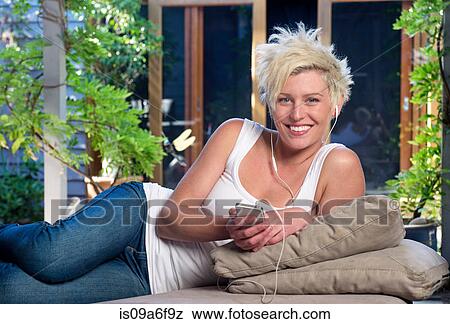 Stock Photo - Young woman on sofa listening to music. Fotosearch