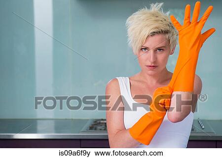 Stock Photo - Young woman putting on orange washing up gloves. Fotosearch