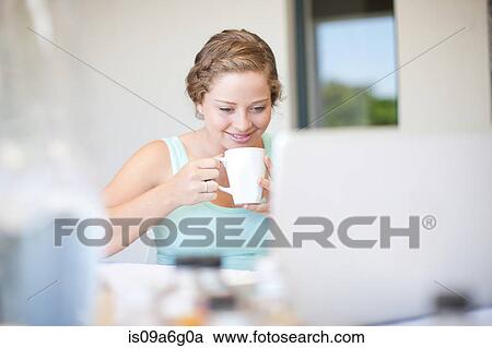Young woman using laptop drinking tea View Large Photo Image Stock Image - Young woman using laptop drinking tea. Fotosearch