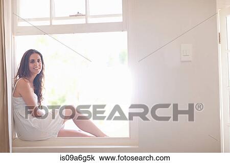 Stock Image - Young woman wearing sundress by window. Fotosearch