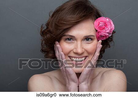 Stock Image - Young woman with flower in hair and hands on face. Fotosearch
