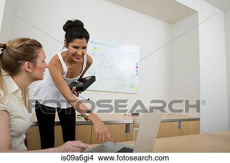 Young women at work, one woman using laptop View Large Photo Image Picture - Young women at work, one woman using laptop. Fotosearch