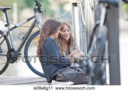 Young women sitting by chain fence with bicycle View Large Photo Image Stock Image - Young women sitting by chain fence with bicycle. Fotosearch