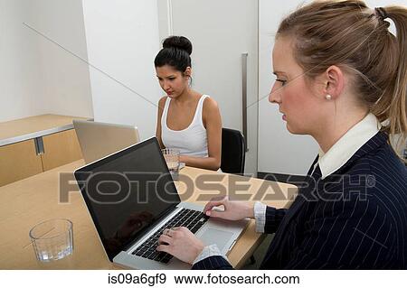 Young women working, one using laptop View Large Photo Image Stock Photo - Young women working, one using laptop. Fotosearch
