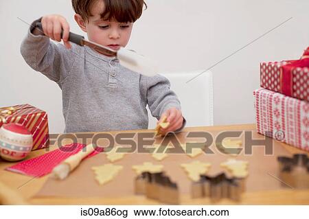 Stock Image - Boy baking Christmas biscuits, holding spatula. Fotosearch