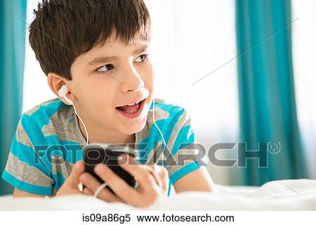 Stock Photography - Boy listening to mp3 player on bed. Fotosearch