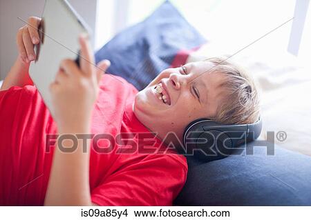 Boy on bed listening to music and using digital tablet View Large Photo Image Picture - Boy on bed listening to music and using digital tablet. Fotosearch