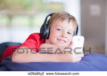 Boy on bed listening to music on smartphone View Large Photo Image Stock Image - Boy on bed listening to music on smartphone. Fotosearch