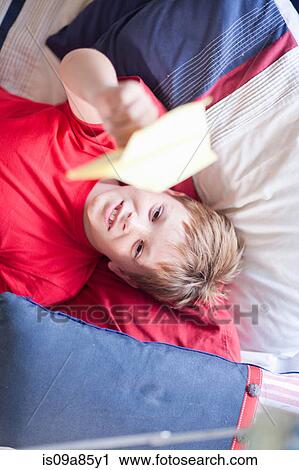 Stock Image - Boy on bed playing with paper aeroplane. Fotosearch