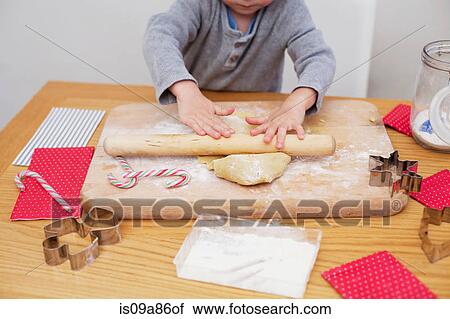 Stock Image - Boy rolling cookie dough, baking Christmas biscuits. Fotosearch