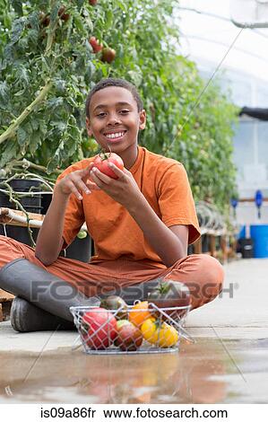 Stock Photography - Boy sitting cross legged holding ripe tomato. Fotosearch