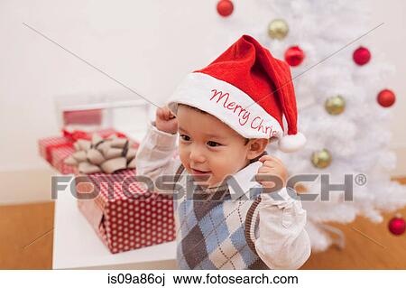 Boy wearing Santa hat in front of Christmas decorations View Large Photo Image Stock Image - Boy wearing Santa hat in front of Christmas decorations. Fotosearch