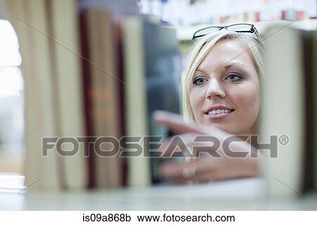 Stock Image - Female student choosing book in library. Fotosearch