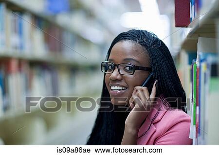 Stock Image - Female student in library using smartphone. Fotosearch
