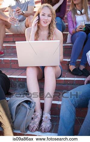 Stock Photo - Female student on steps using laptop on cell phone. Fotosearch