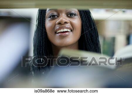 Stock Image - Female student peering between books. Fotosearch