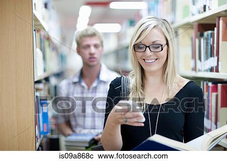 Female student using smartphone in library, man in background View Large Photo Image Stock Image - Female student using smartphone in library, man in background. Fotosearch