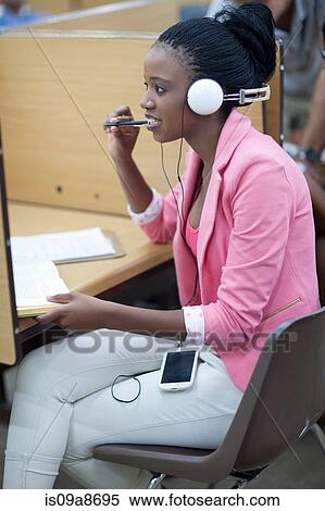 Stock Photography - Female student working in library with headphones. Fotosearch