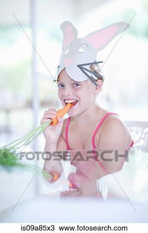 Stock Image - Girl in rabbit costume eating carrot. Fotosearch
