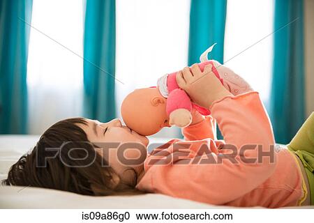 Stock Image - Girl kissing dolly in bedroom. Fotosearch