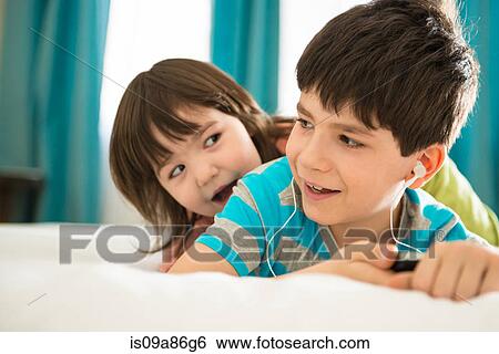Stock Photograph - Girl looking at boy listening to mp3 player on bed. Fotosearch