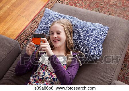 Girl lying on sofa playing handheld video game View Large Photo Image Stock Photograph - Girl lying on sofa playing handheld video game. Fotosearch