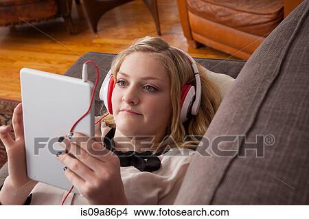 Picture - Girl lying on sofa using digital tablet. Fotosearch