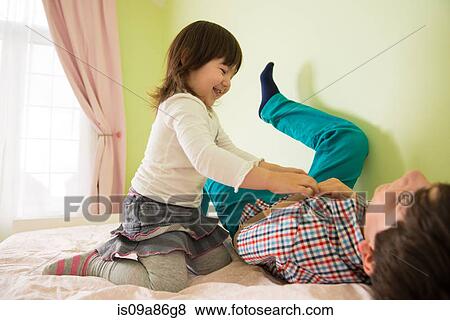 Stock Photo - Girl tickling brother on bed. Fotosearch