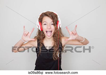 Girl wearing headphones making devil signs and sticking tongue out View Large Photo Image Stock Image - Girl wearing headphones making devil signs and sticking tongue out. Fotosearch