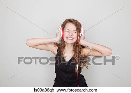 Stock Image - Girl wearing headphones with hands over ears. Fotosearch
