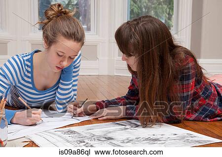 Stock Image - Girls lying on floor drawing pictures. Fotosearch
