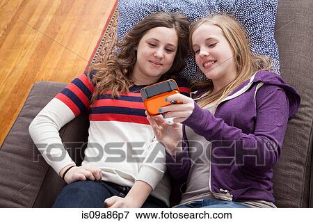 Stock Photo - Girls lying on sofa playing handheld video game. Fotosearch