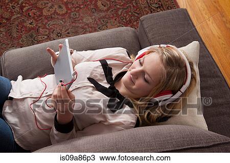 Stock Image - Girls lying on sofa using digital tablet. Fotosearch