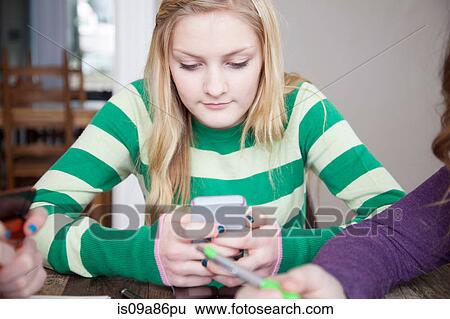 Stock Photograph - Girls sitting at table using smart phone. Fotosearch